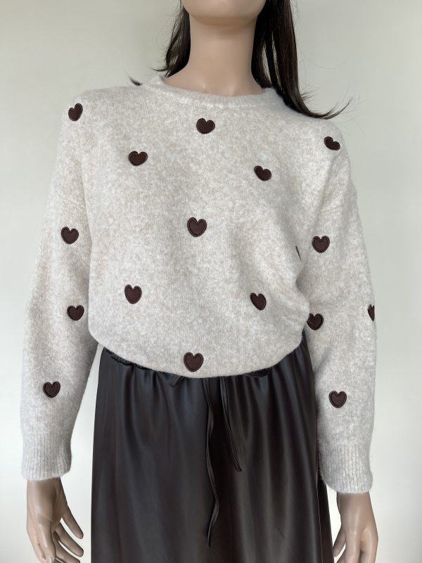 Beige trui met donkerbruine hartjes. De trui heeft een ronde hals. Gemaakt van een zachte stof die comfortabel aanvoelt.